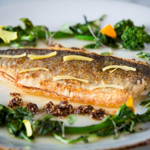 A close-up of a grilled sandwich topped with herbs, served on a plate with greens and a lemon wedge, steam rising from the hot, melty filling.