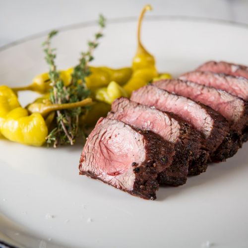 A sliced roasted beef fillet with a lemony side and greens, artistically plated.
