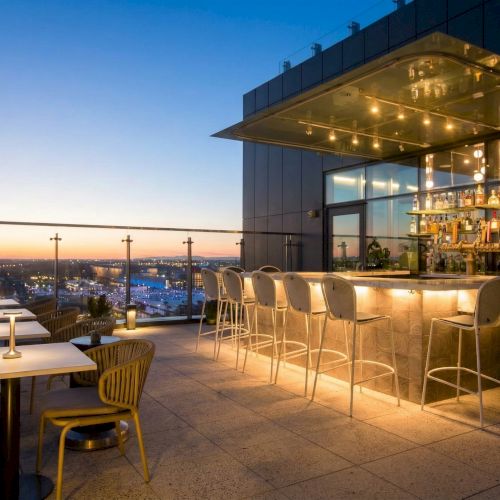 A cozy lakeside caf&eacute; with wooden deck, warm lights, and a thatched roof hut; waterfront views and a calm evening vibe.